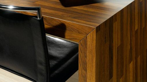 Detailaufnahme eines Esstisches aus dunklem Massivholz in Kombination mit Ledersessel