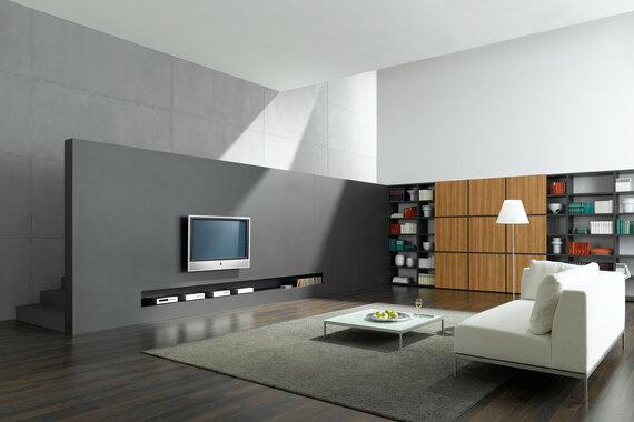 Offene Wohnraumimpression mit grauer TV-Trennwand zur Treppe und Einbauregal aus Holz und weißem Sofa